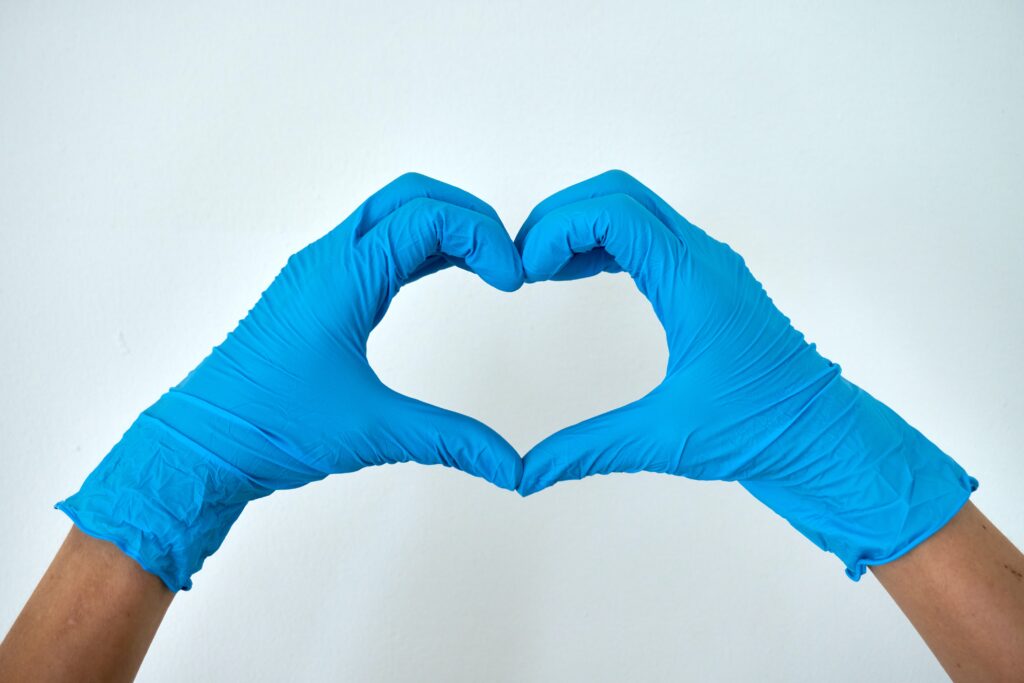 A person wearing medical blue gloves, makes a heart shape with their hands.
