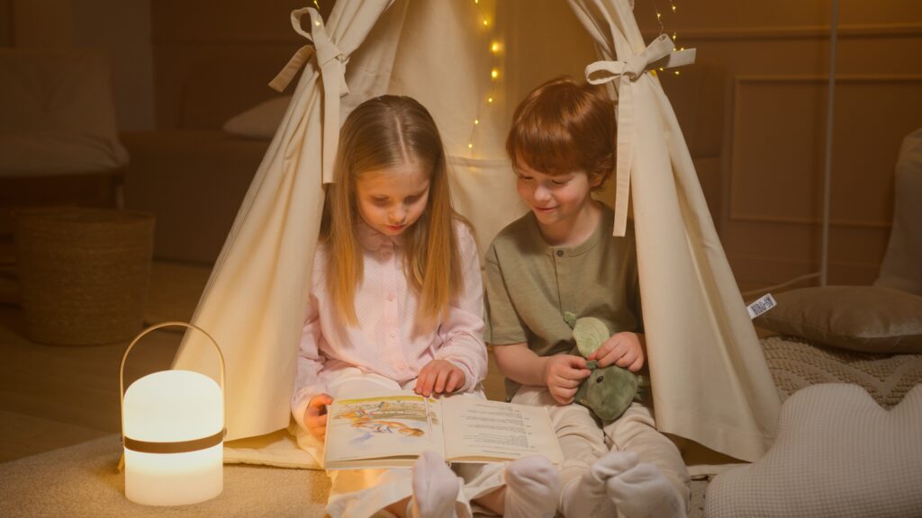 Two kids sitting and reading under a tent decorated with Christmas lights that sensory support them.
